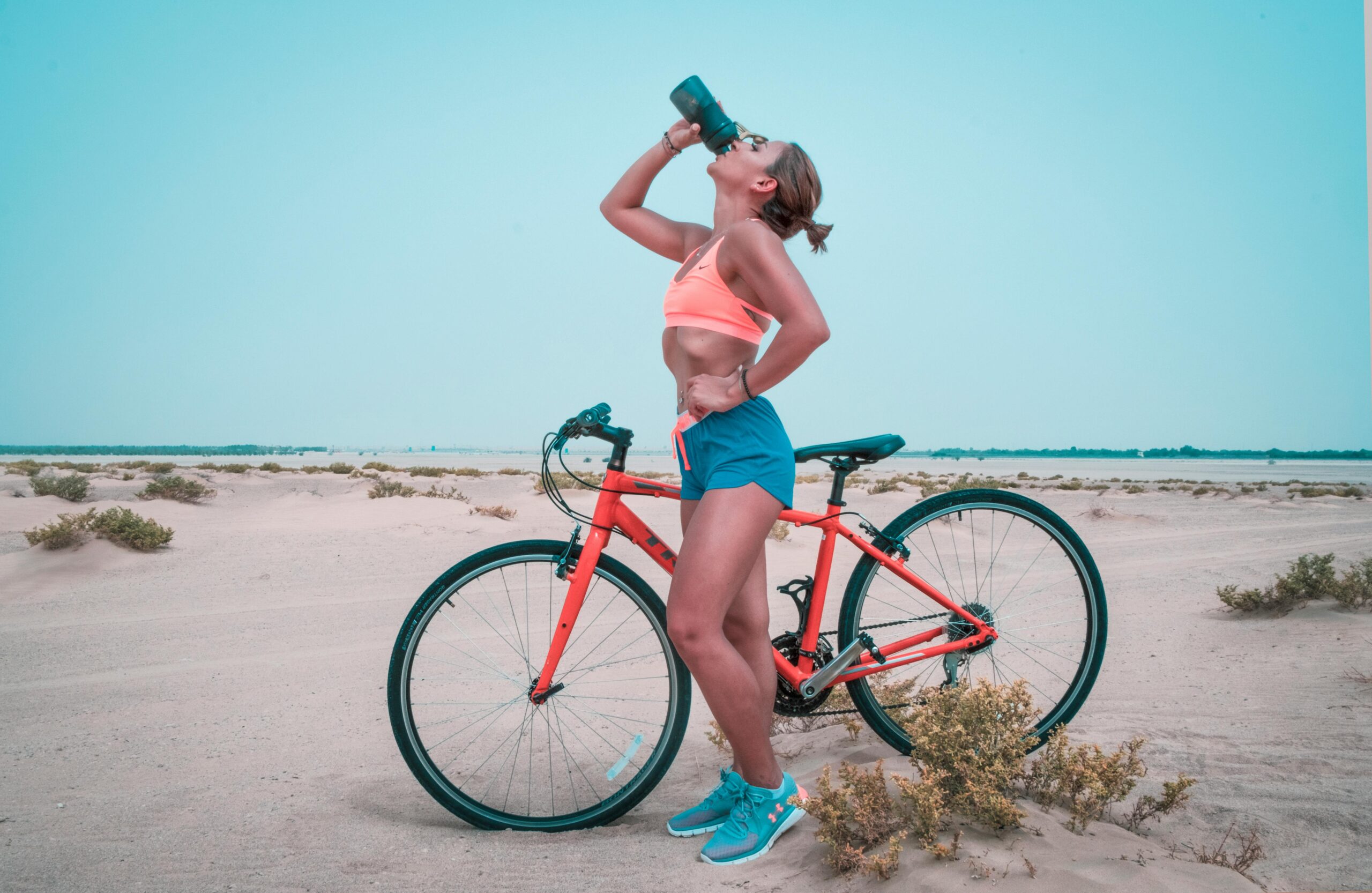 Woman drinking water by a bike near a beach for Integrating Genetic Insights post